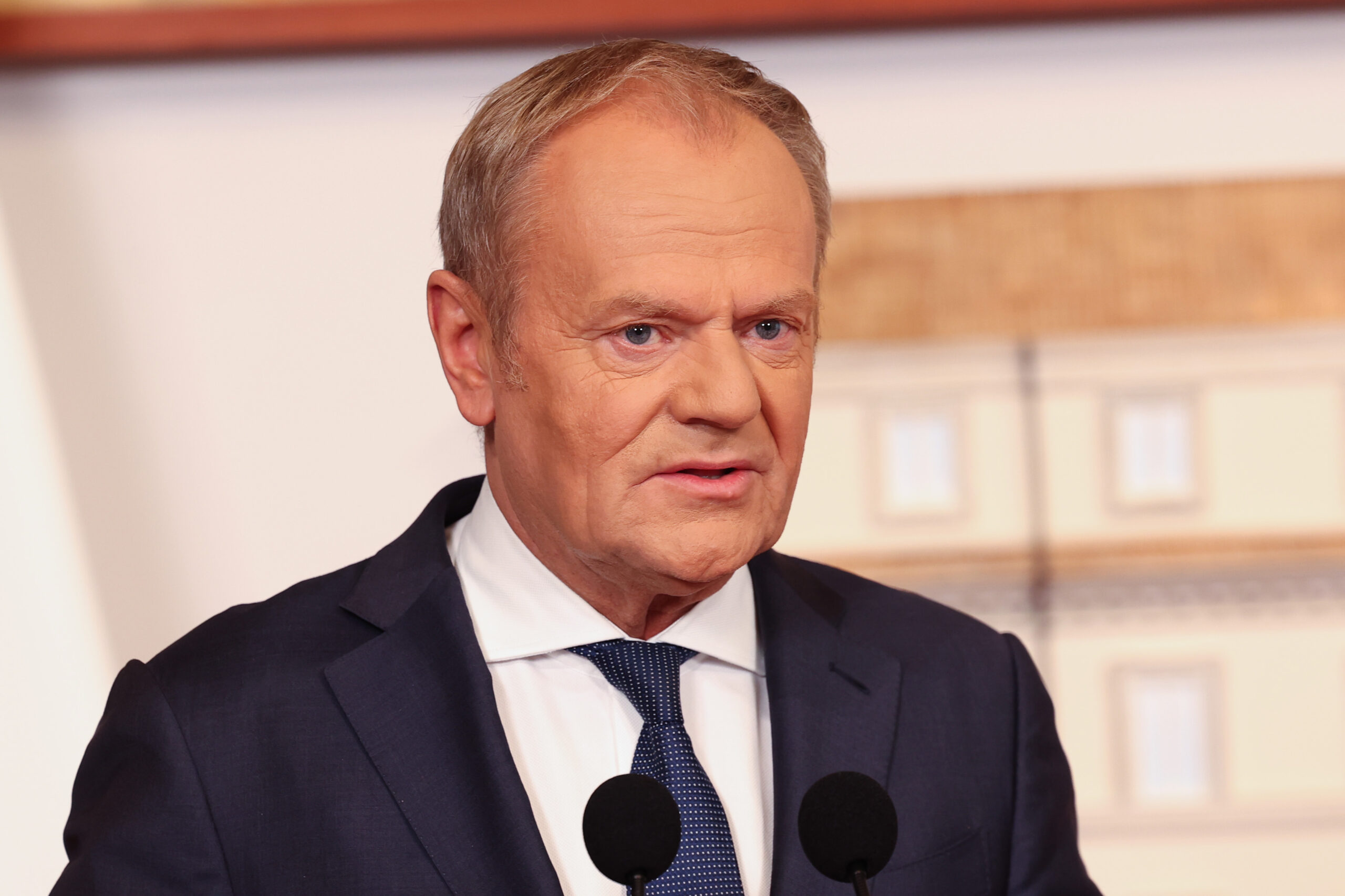 Чоловік у темному костюмі говорить перед двома мікрофонами
